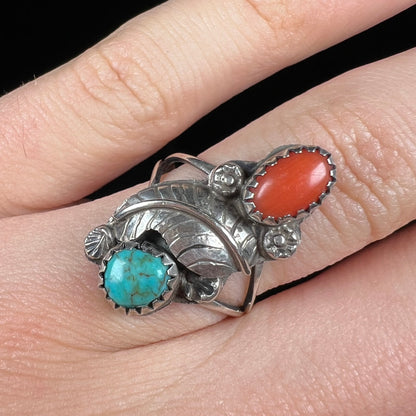 A vintage sterling silver Navajo style ring set with turquoise and coral stones and a feather design.