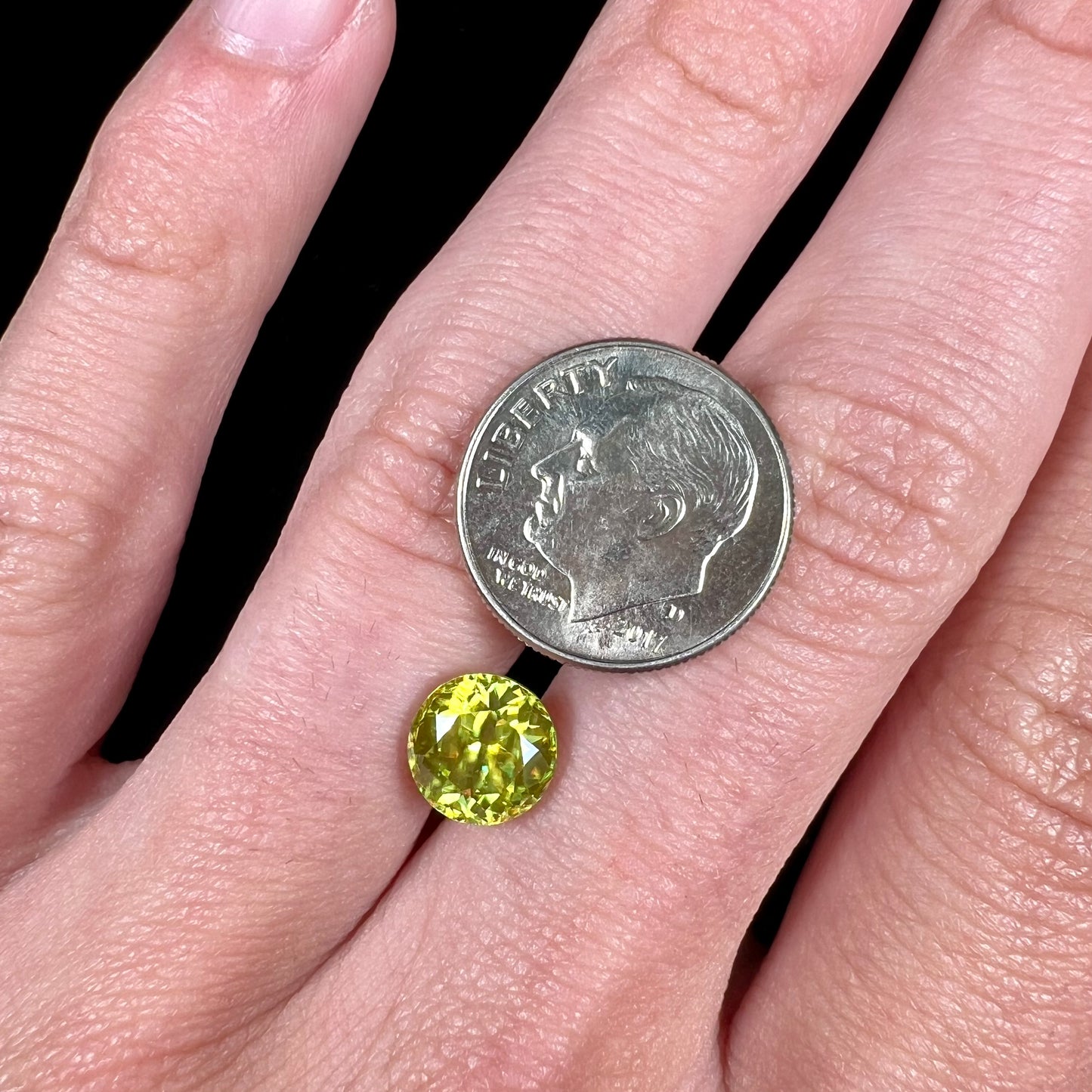 A loose, round brilliant cut sphene gemstone.  The stone is green with orange, green, blue, and yellow flashes.