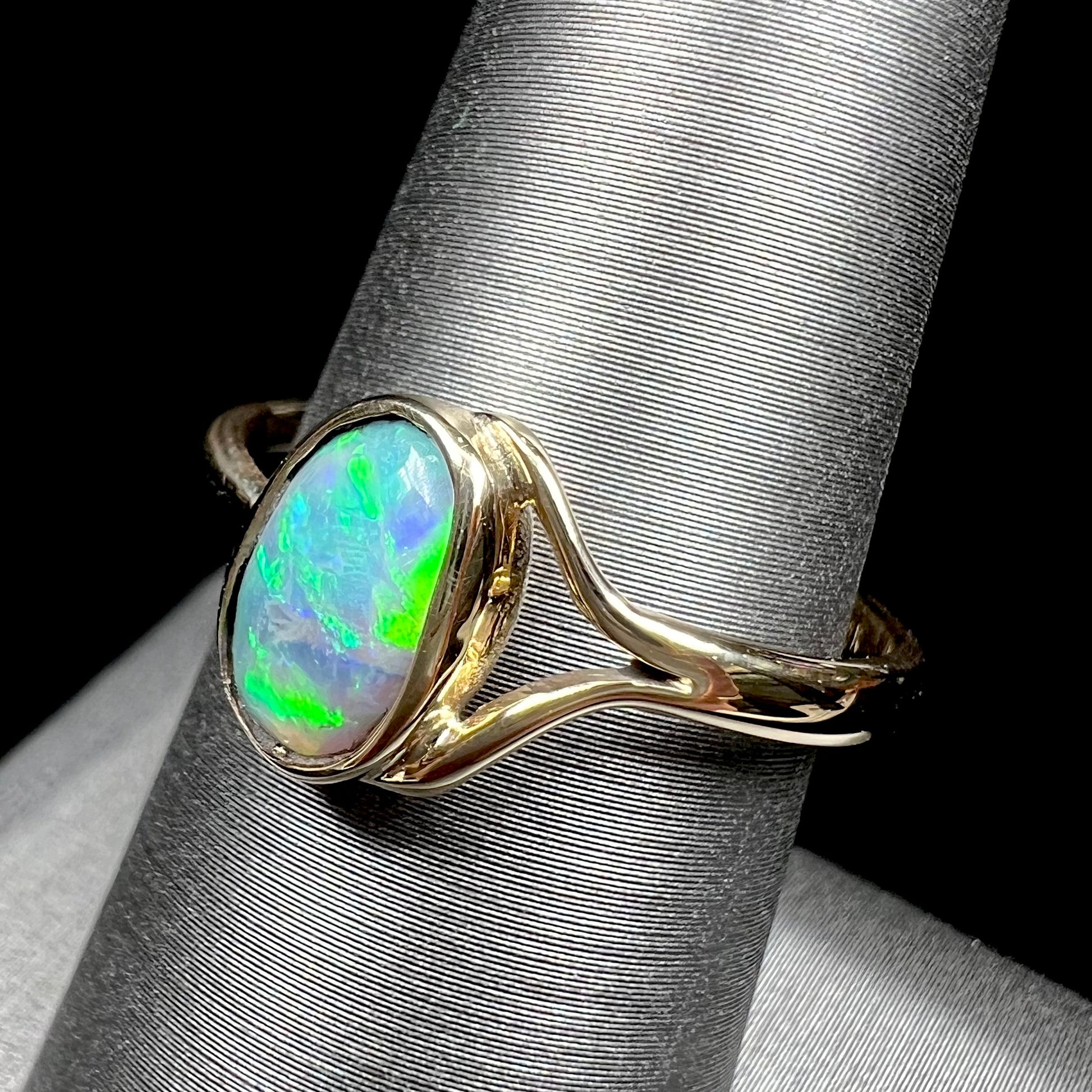 A ladies' oval cut black crystal opal solitaire ring handmade with a single split shank in yellow gold.