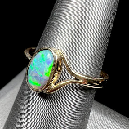 A ladies' oval cut black crystal opal solitaire ring handmade with a single split shank in yellow gold.