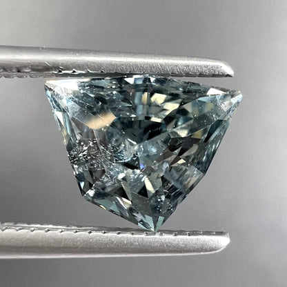 A loose, freeform shield cut tourmaline gemstone.  The stone is a steel blue color.