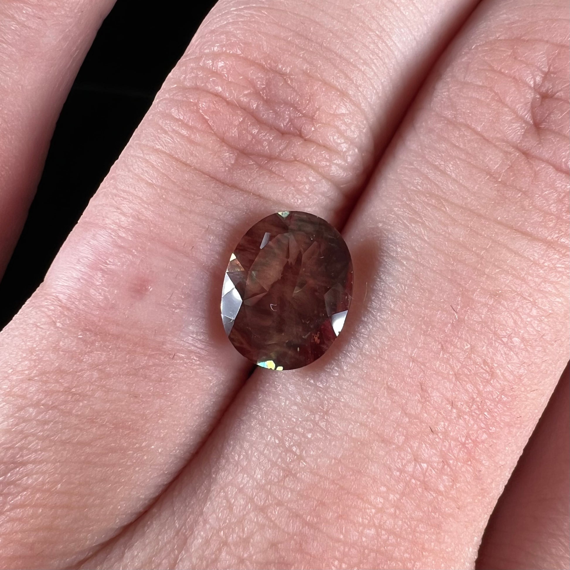 A loose, oval cut oregon sunstone.  The gem is reddish orange with a green secondary color.