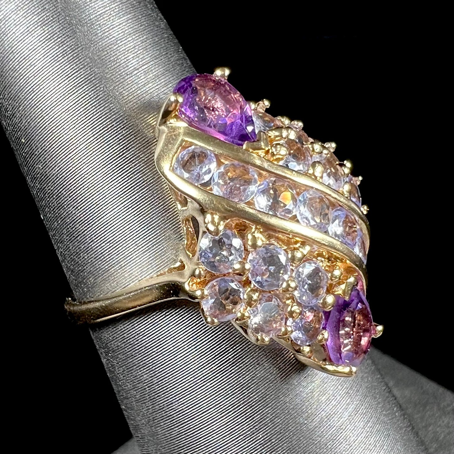 A ladies' gold ring set with a cluster of round tanzanites and two pear shaped amethyst accent stones.