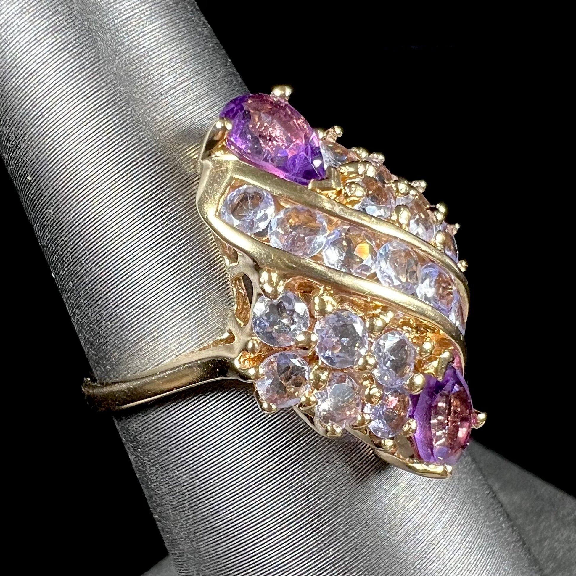 A ladies' gold ring set with a cluster of round tanzanites and two pear shaped amethyst accent stones.