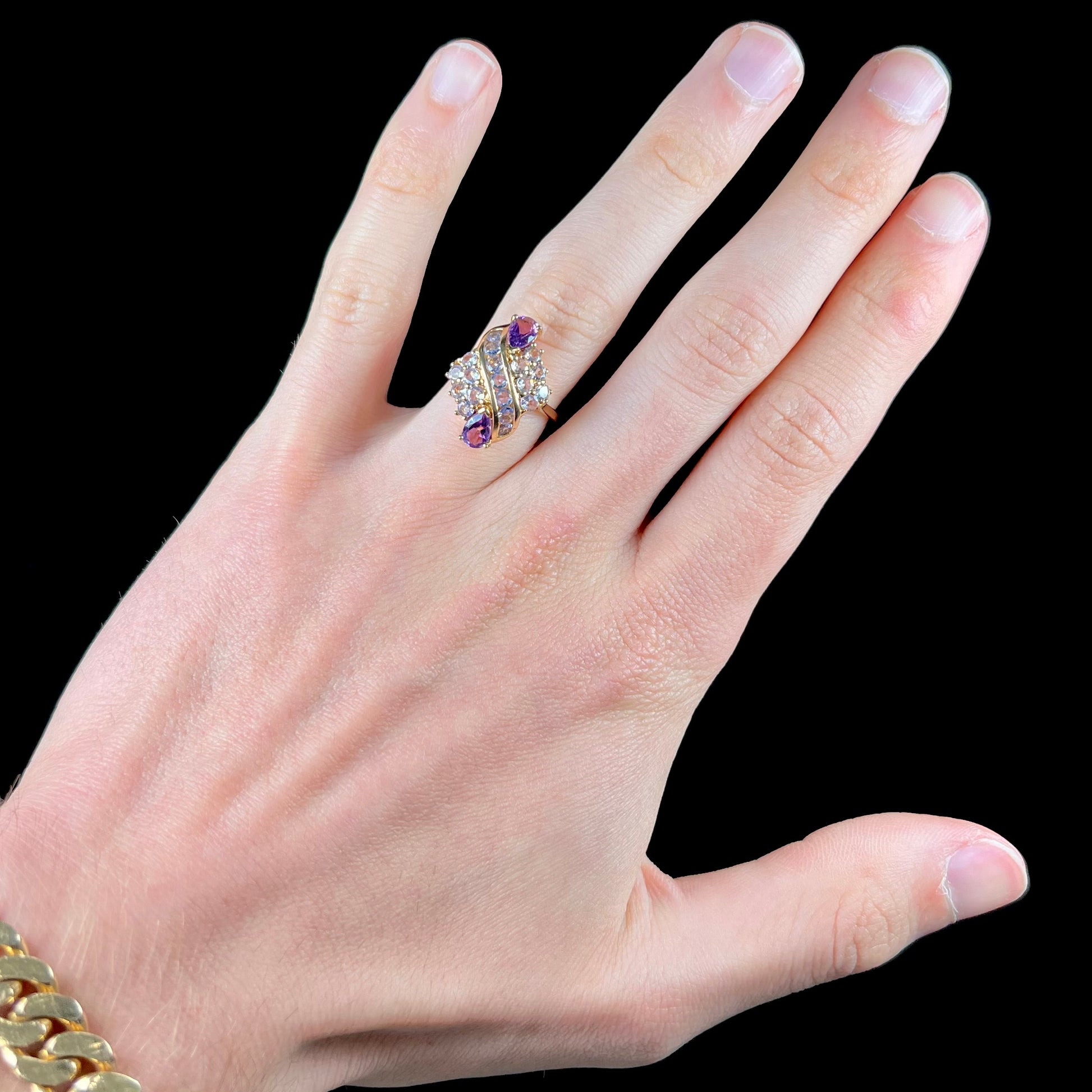 A ladies' gold ring set with a cluster of round tanzanites and two pear shaped amethyst accent stones.