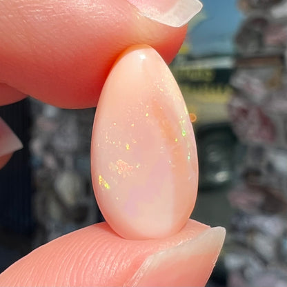 A loose, pear shaped pink Peruvian opal cabochon.  The opal has green play of color.
