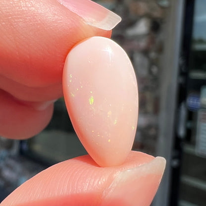 A loose, pear shaped pink Peruvian opal cabochon.  The opal has green play of color.