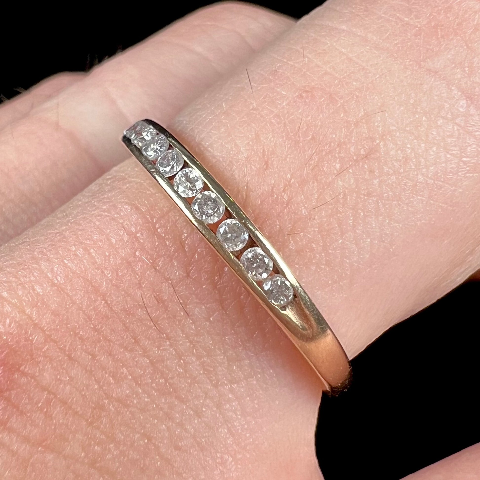 A unisex, thin yellow gold wedding band channel set with 12 round cut diamonds.