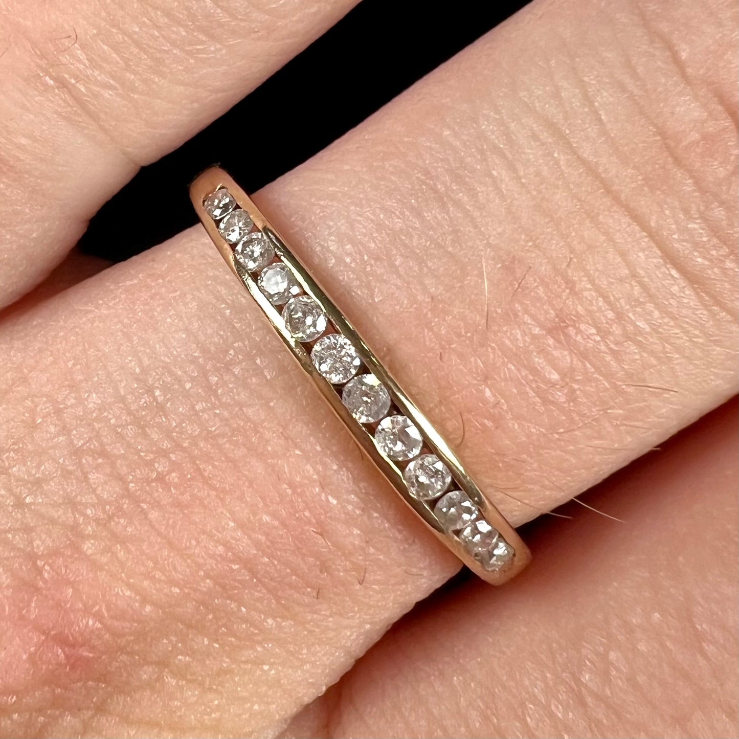 A unisex, thin yellow gold wedding band channel set with 12 round cut diamonds.