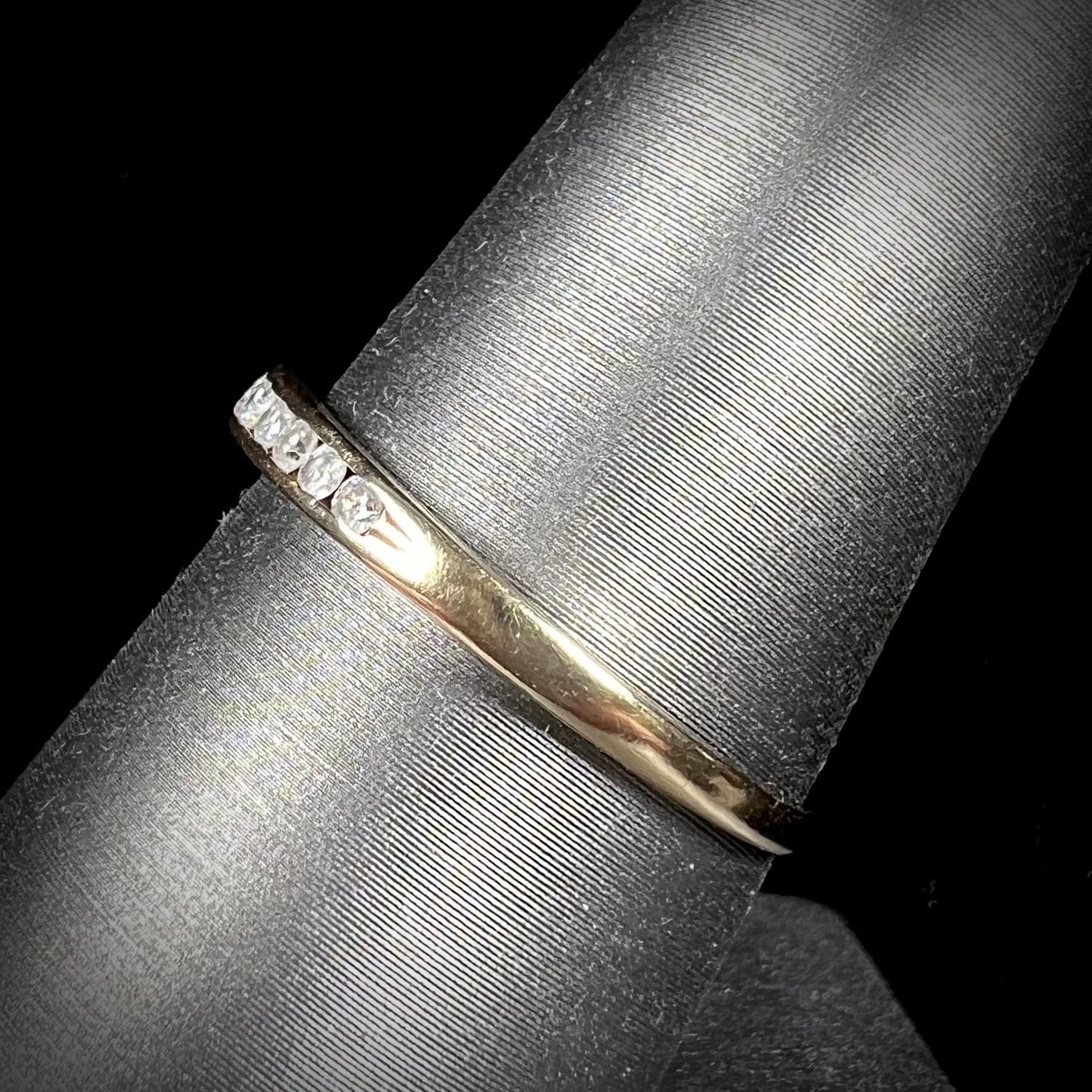 A unisex, thin yellow gold wedding band channel set with 12 round cut diamonds.