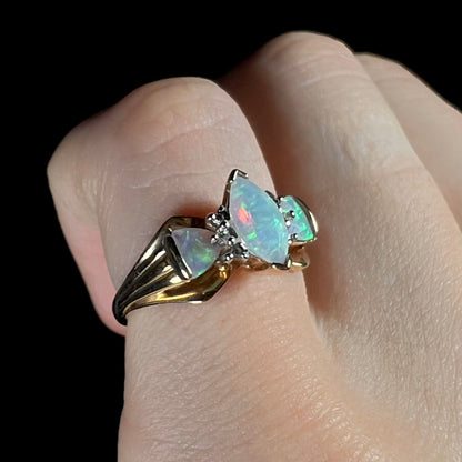 A yellow gold, diamond accented ring set with a marquise cut and two trillion cut lab created opals.