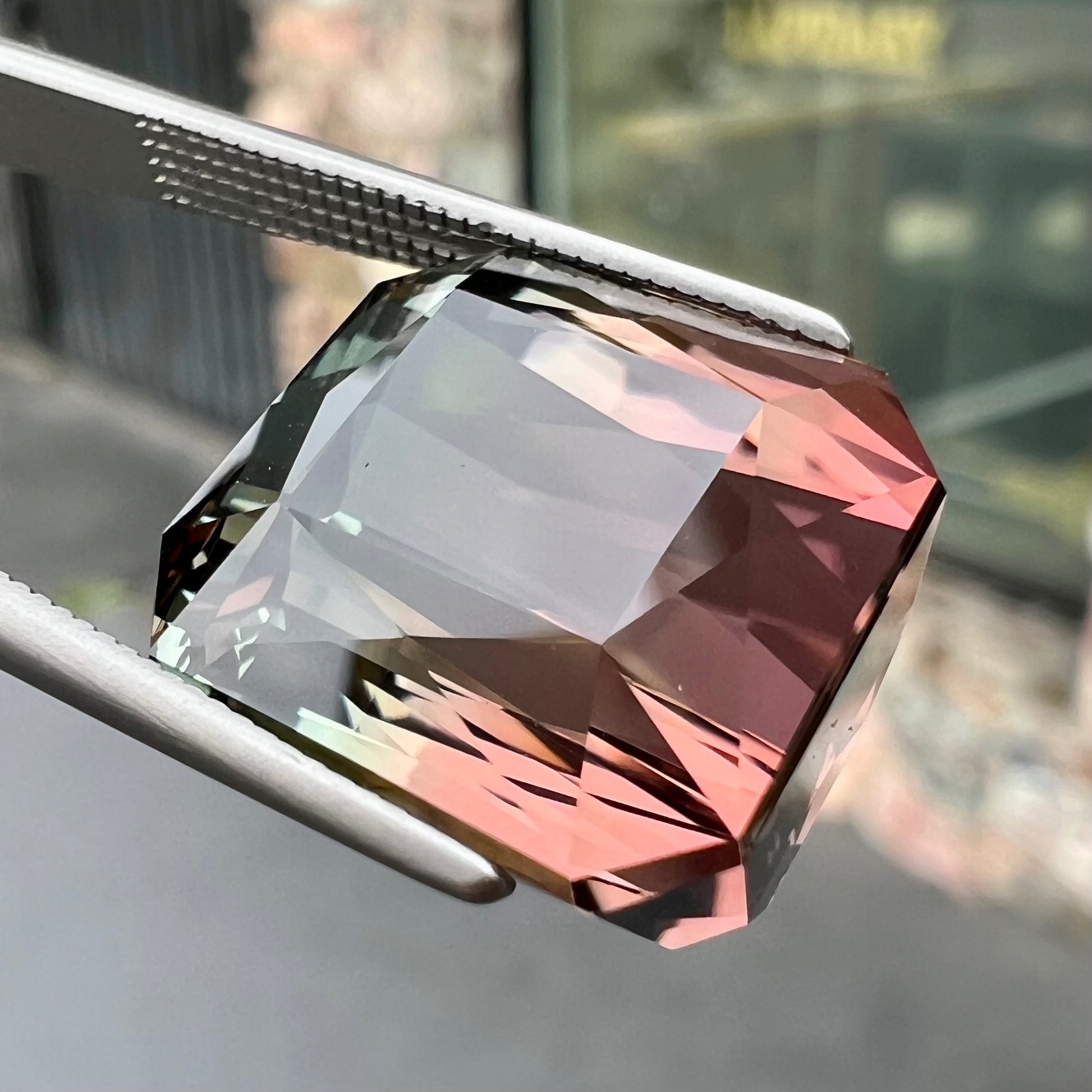 A loose, faceted modified emerald cut bicolor tourmaline gemstone.  The stone transitions from dark pink to dark green colors.
