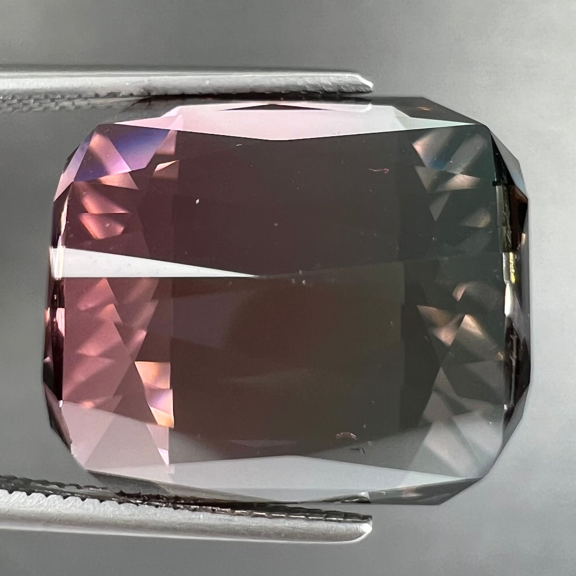 A loose, faceted modified emerald cut bicolor tourmaline gemstone.  The stone transitions from dark pink to dark green colors.
