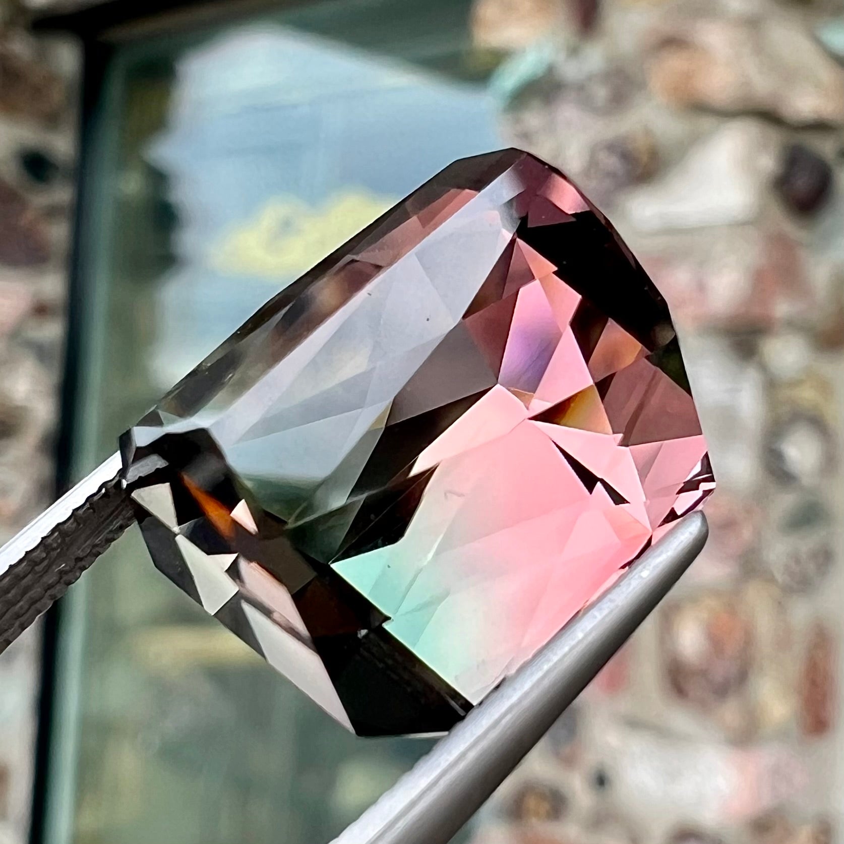 A loose, faceted modified emerald cut bicolor tourmaline gemstone.  The stone transitions from dark pink to dark green colors.