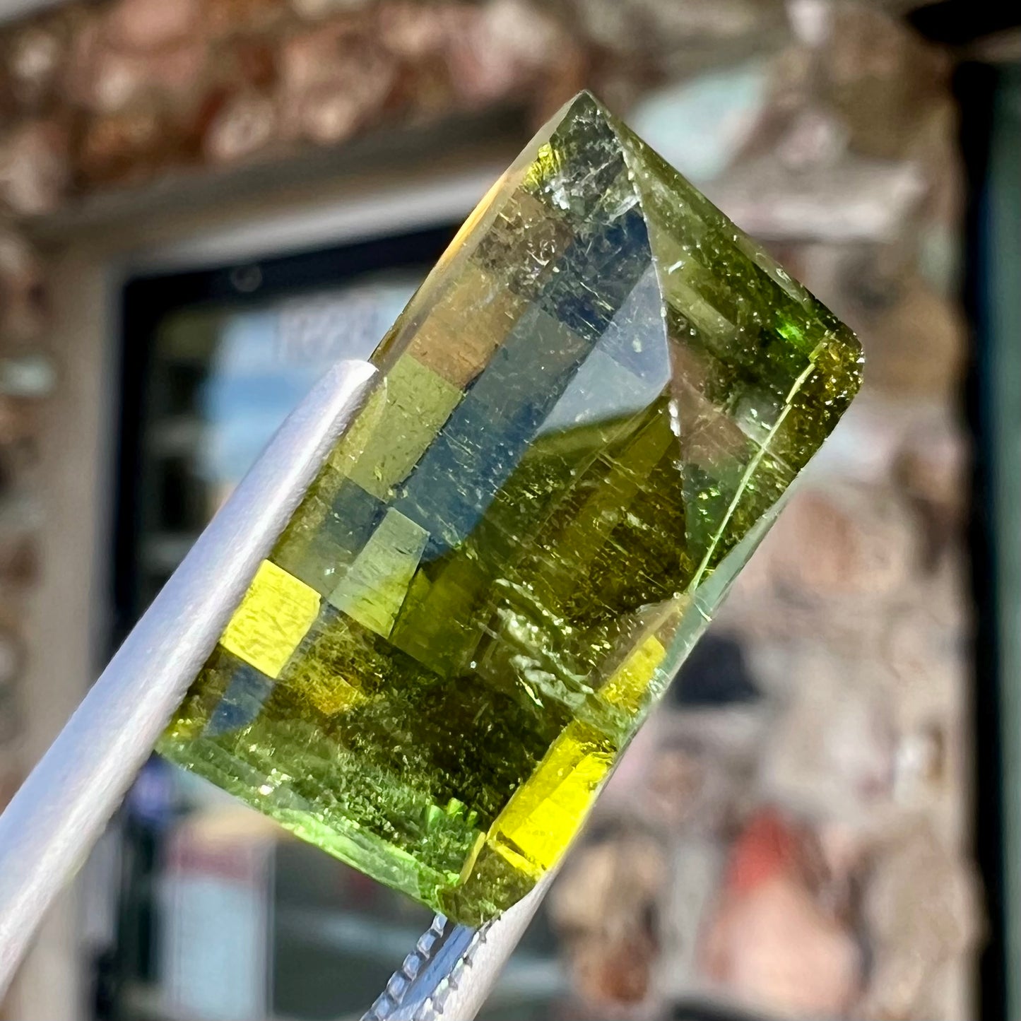 A rectangular step-cut yellowish green tourmaline gemstone.
