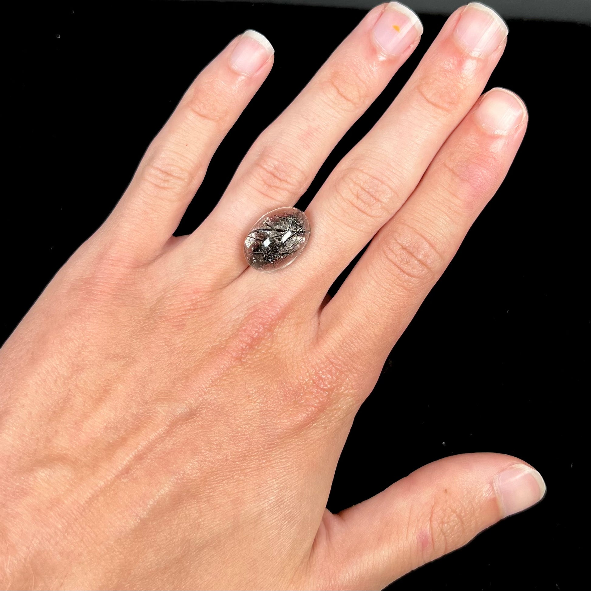A loose, oval cabochon cut clear quartz stone with black tourmaline needle inclusions.