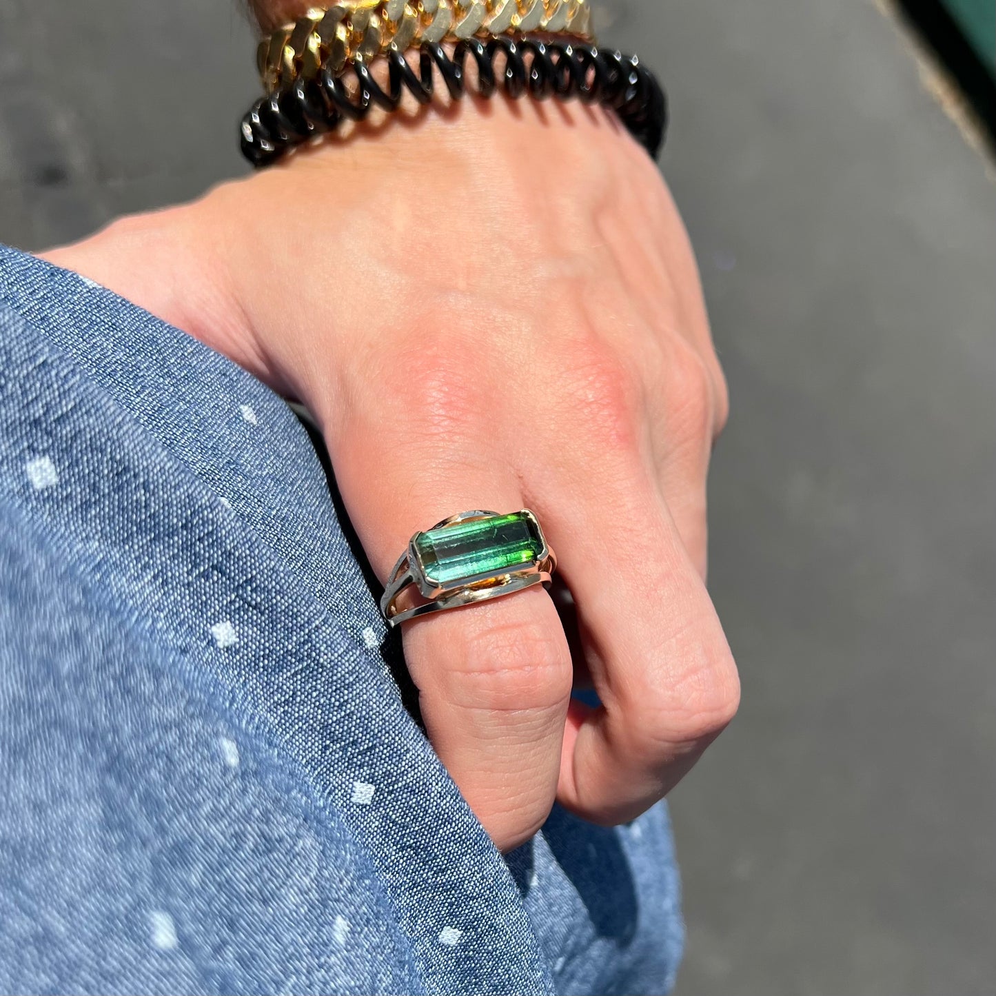 A men's emerald cut tricolor tourmaline solitaire ring in yellow gold.  The tourmaline shifts from green to blue green to blue.