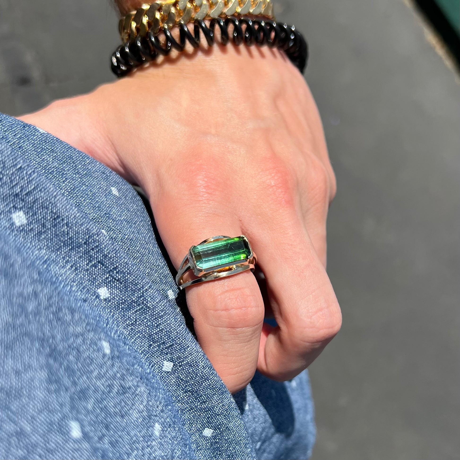 A men's emerald cut tricolor tourmaline solitaire ring in yellow gold.  The tourmaline shifts from green to blue green to blue.