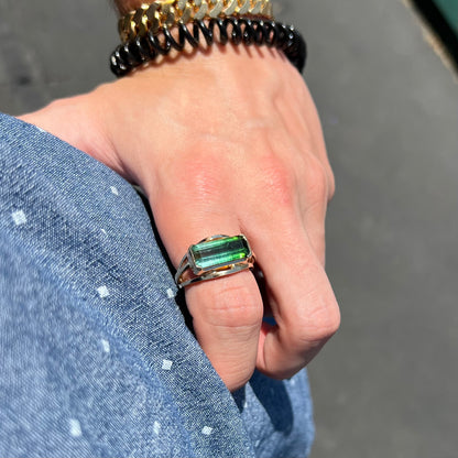 A men's emerald cut tricolor tourmaline solitaire ring in yellow gold.  The tourmaline shifts from green to blue green to blue.