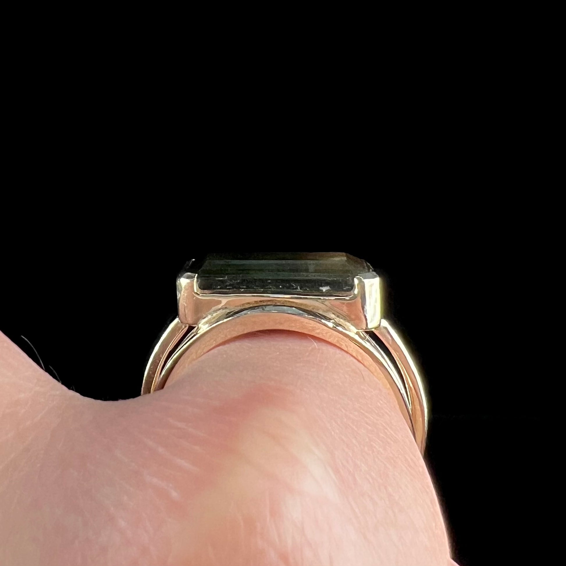 A men's emerald cut tricolor tourmaline solitaire ring in yellow gold.  The tourmaline shifts from green to blue green to blue.