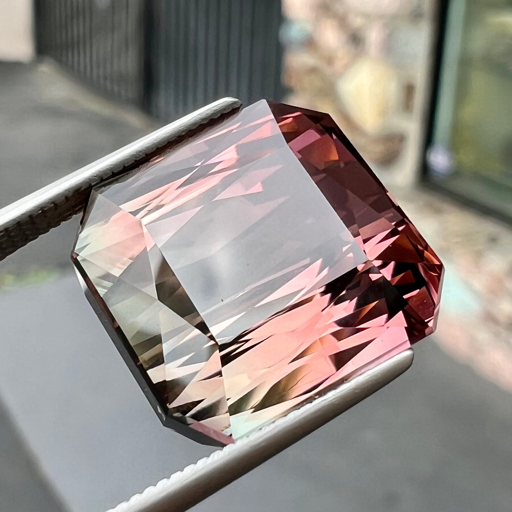 A loose, faceted modified emerald cut bicolor tourmaline gemstone.  The stone transitions from dark pink to dark green colors.