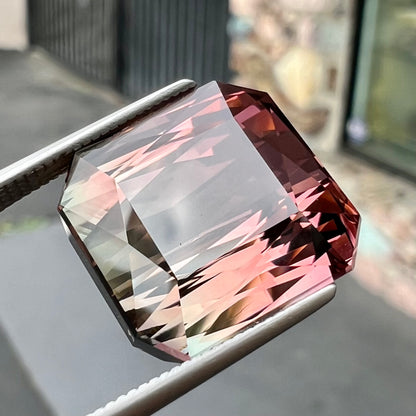 A loose, faceted modified emerald cut bicolor tourmaline gemstone.  The stone transitions from dark pink to dark green colors.