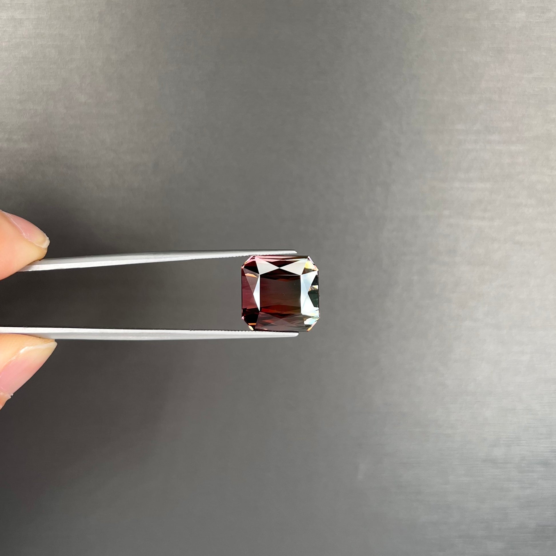 A loose, faceted modified emerald cut bicolor tourmaline gemstone.  The stone transitions from dark pink to dark green colors.
