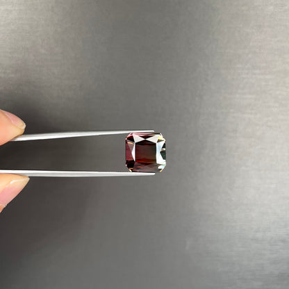 A loose, faceted modified emerald cut bicolor tourmaline gemstone.  The stone transitions from dark pink to dark green colors.