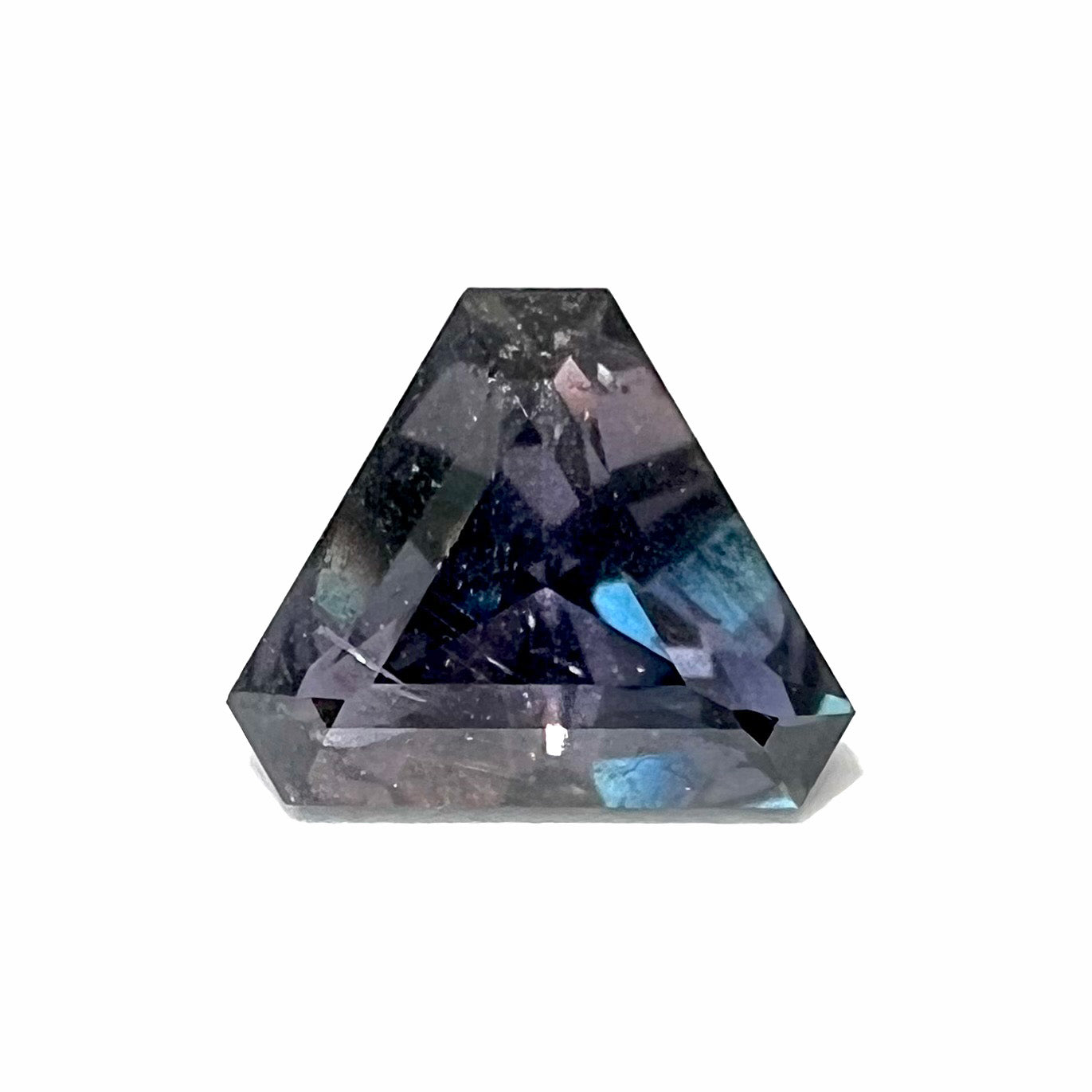 A loose, modified triangle cut parti sapphire gemstone.  The sapphire shows colors of blue, violet, purple, and gray.