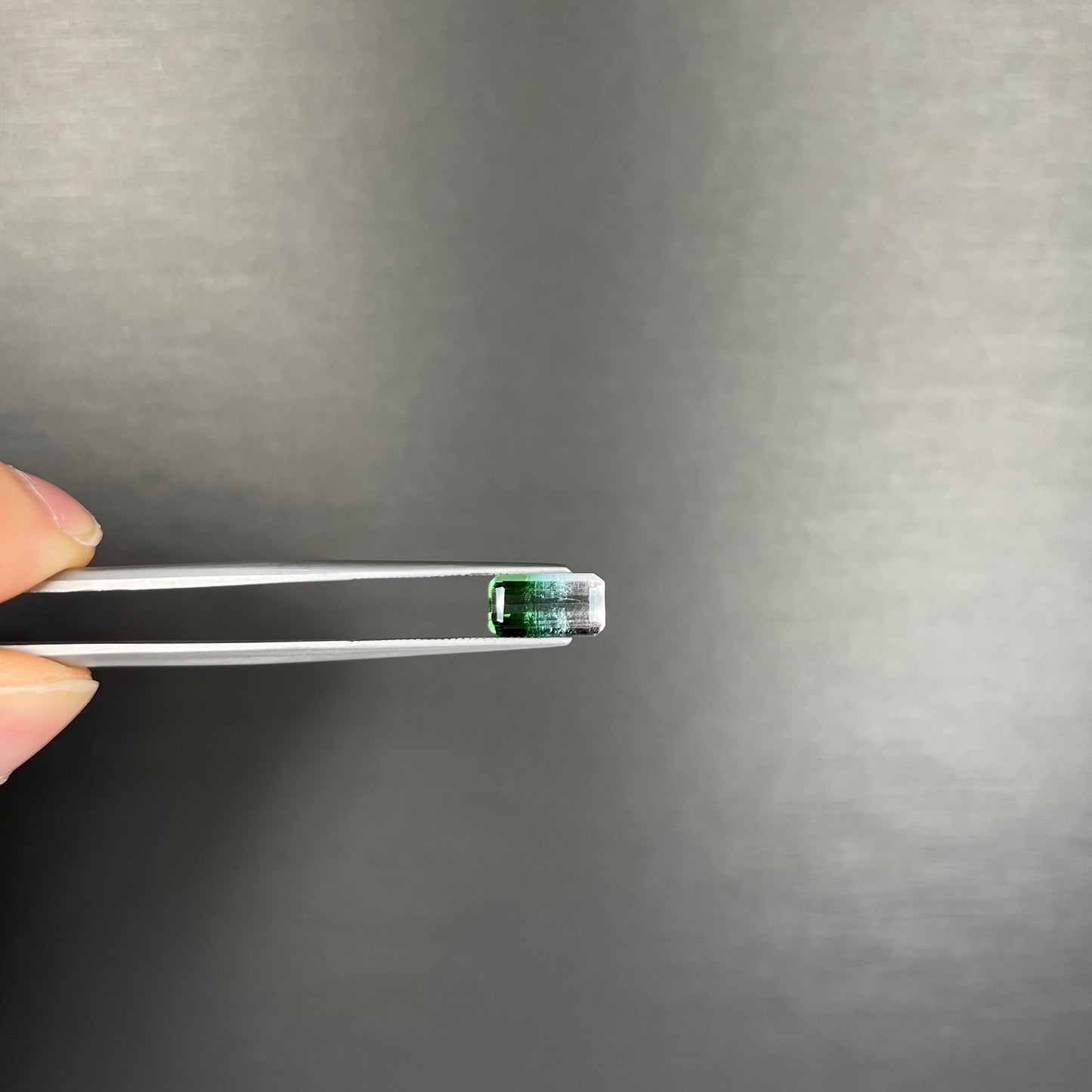 A loose, emerald cut tricolor tourmaline gemstone.  The stone transitions from green to blue to white colors.