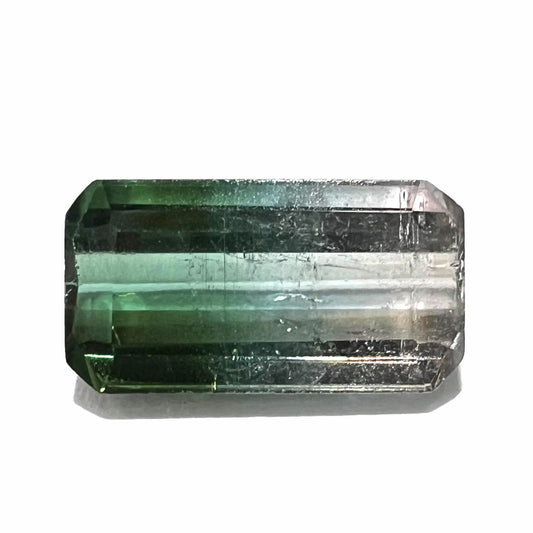 A loose, emerald cut tricolor tourmaline gemstone.  The stone transitions from green to blue to white colors.
