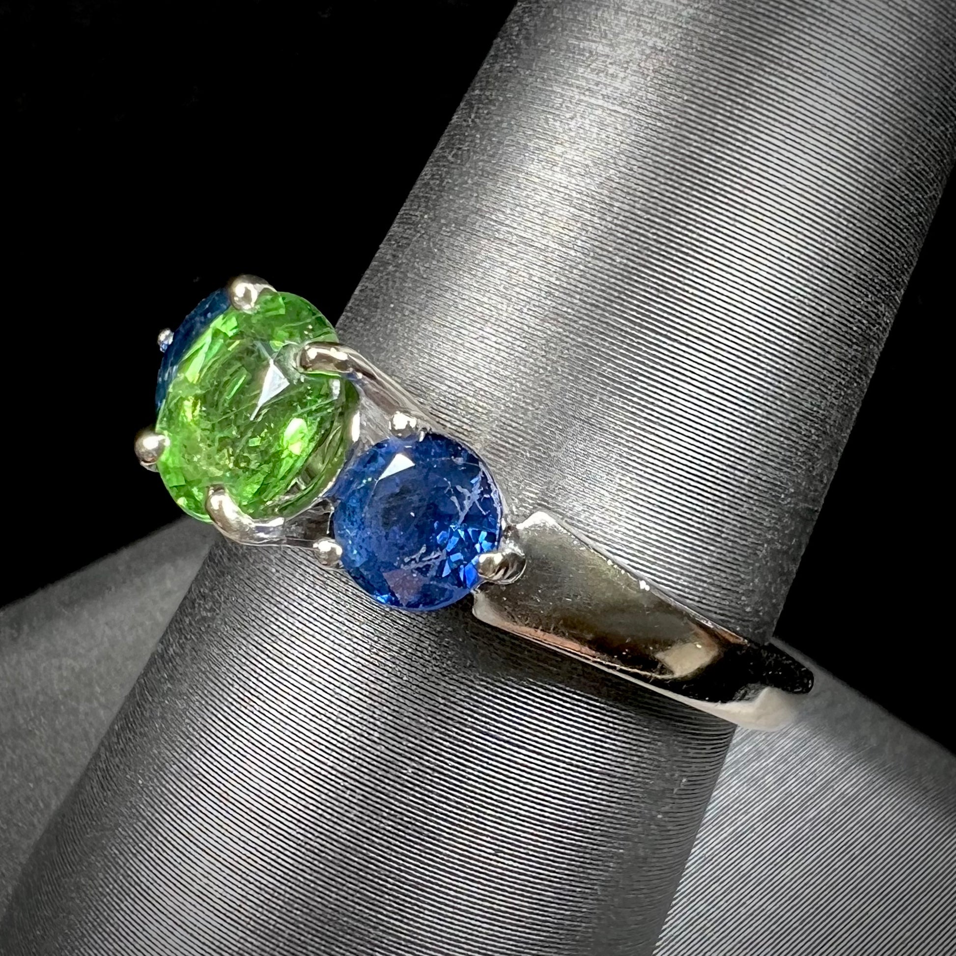 A ladies' white gold three stone ring set with two round blue sapphires and an oval cut green tsavorite garnet.