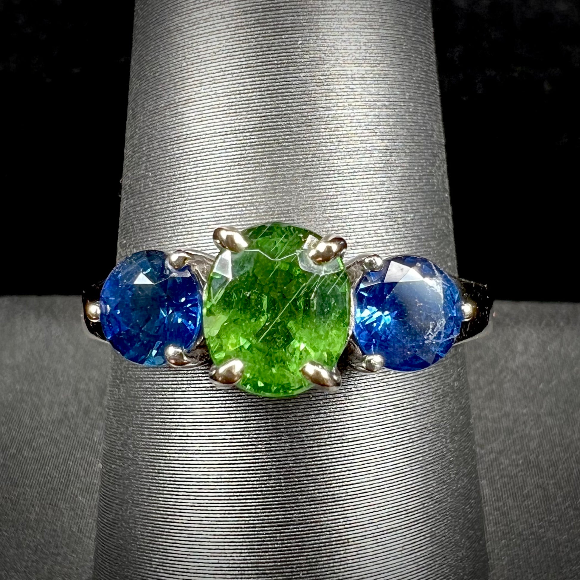 A ladies' white gold three stone ring set with two round blue sapphires and an oval cut green tsavorite garnet.