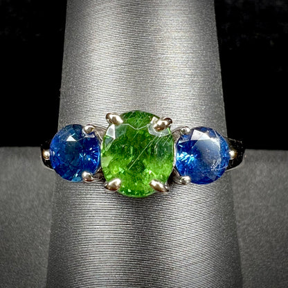 A ladies' white gold three stone ring set with two round blue sapphires and an oval cut green tsavorite garnet.
