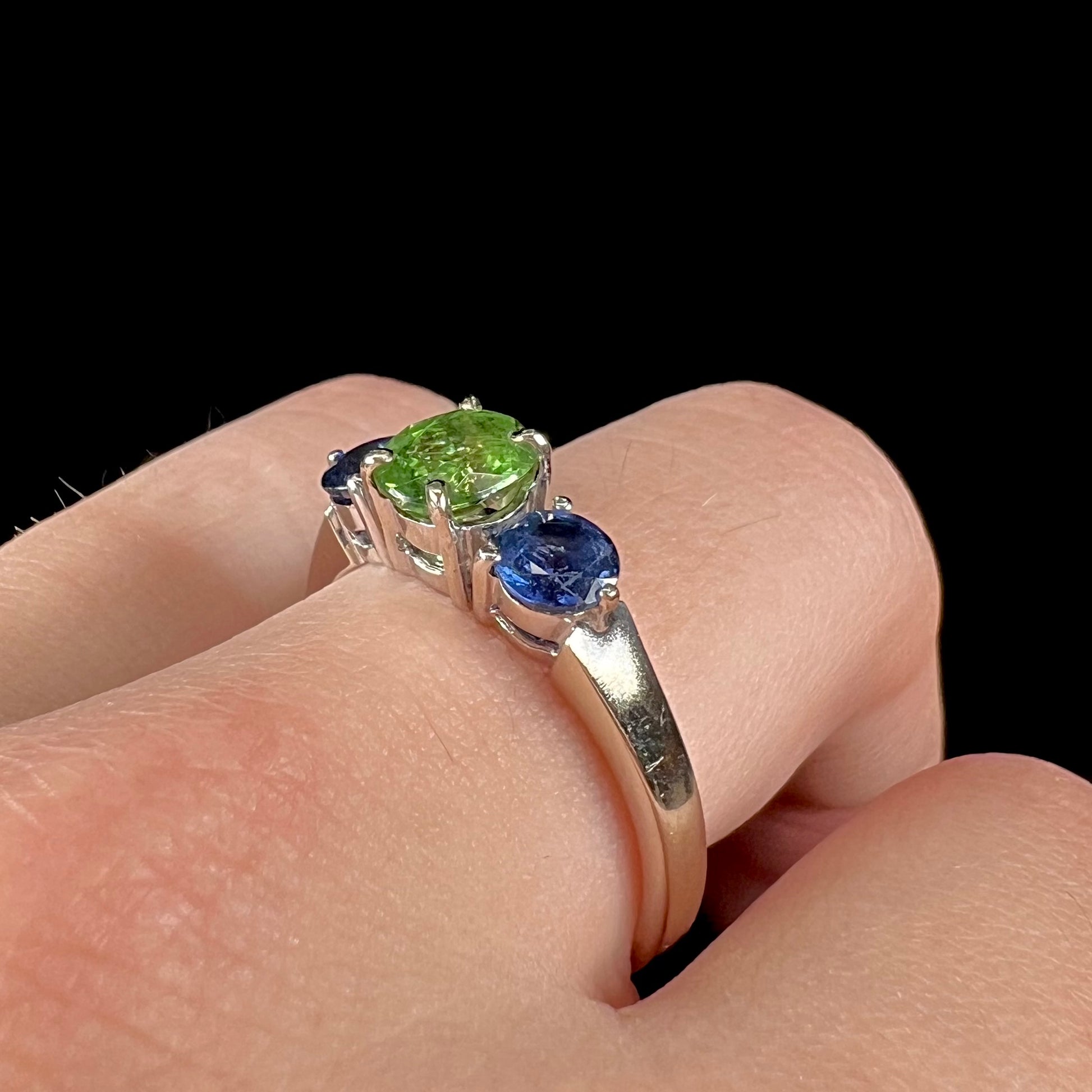 A ladies' white gold three stone ring set with two round blue sapphires and an oval cut green tsavorite garnet.
