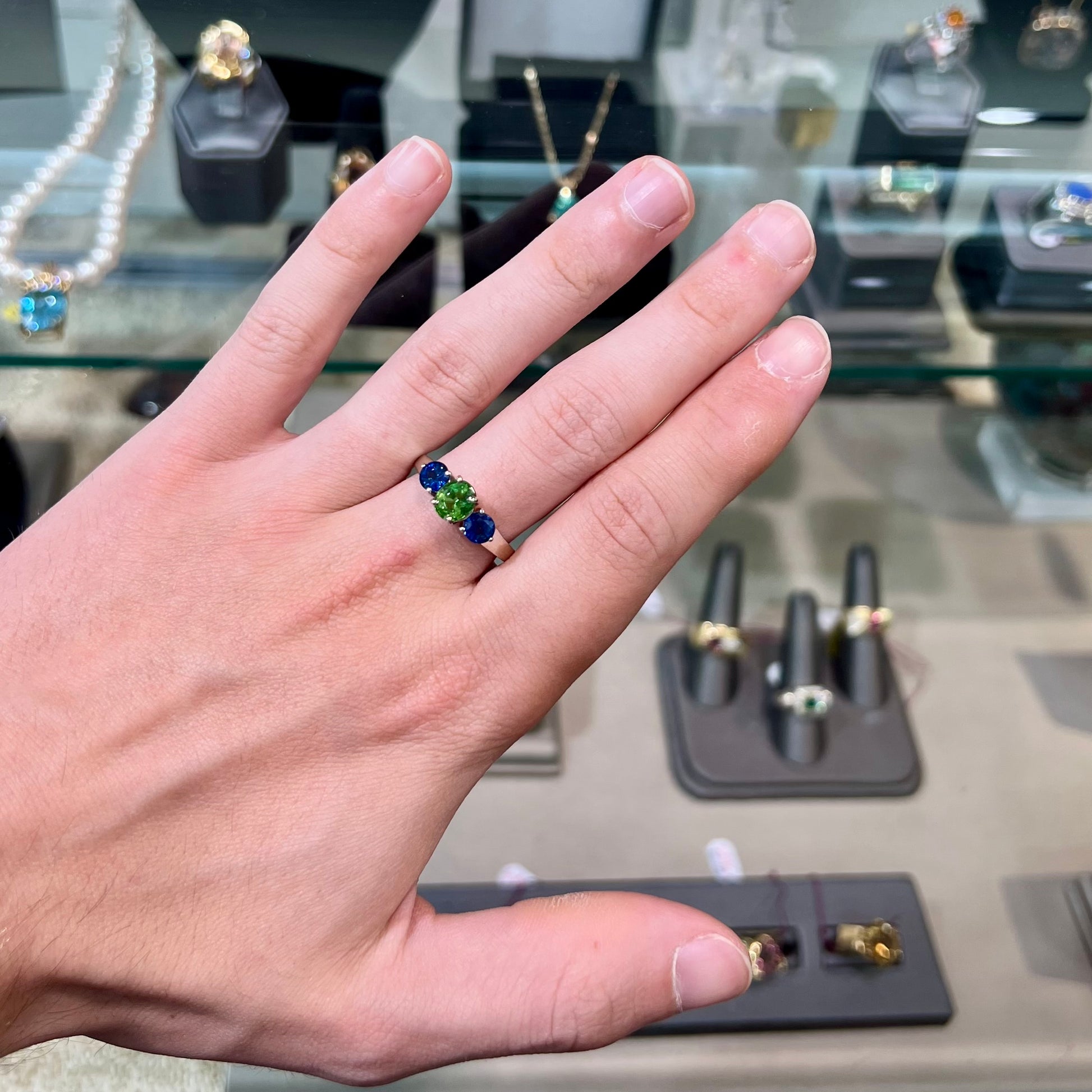 A ladies' white gold three stone ring set with two round blue sapphires and an oval cut green tsavorite garnet.