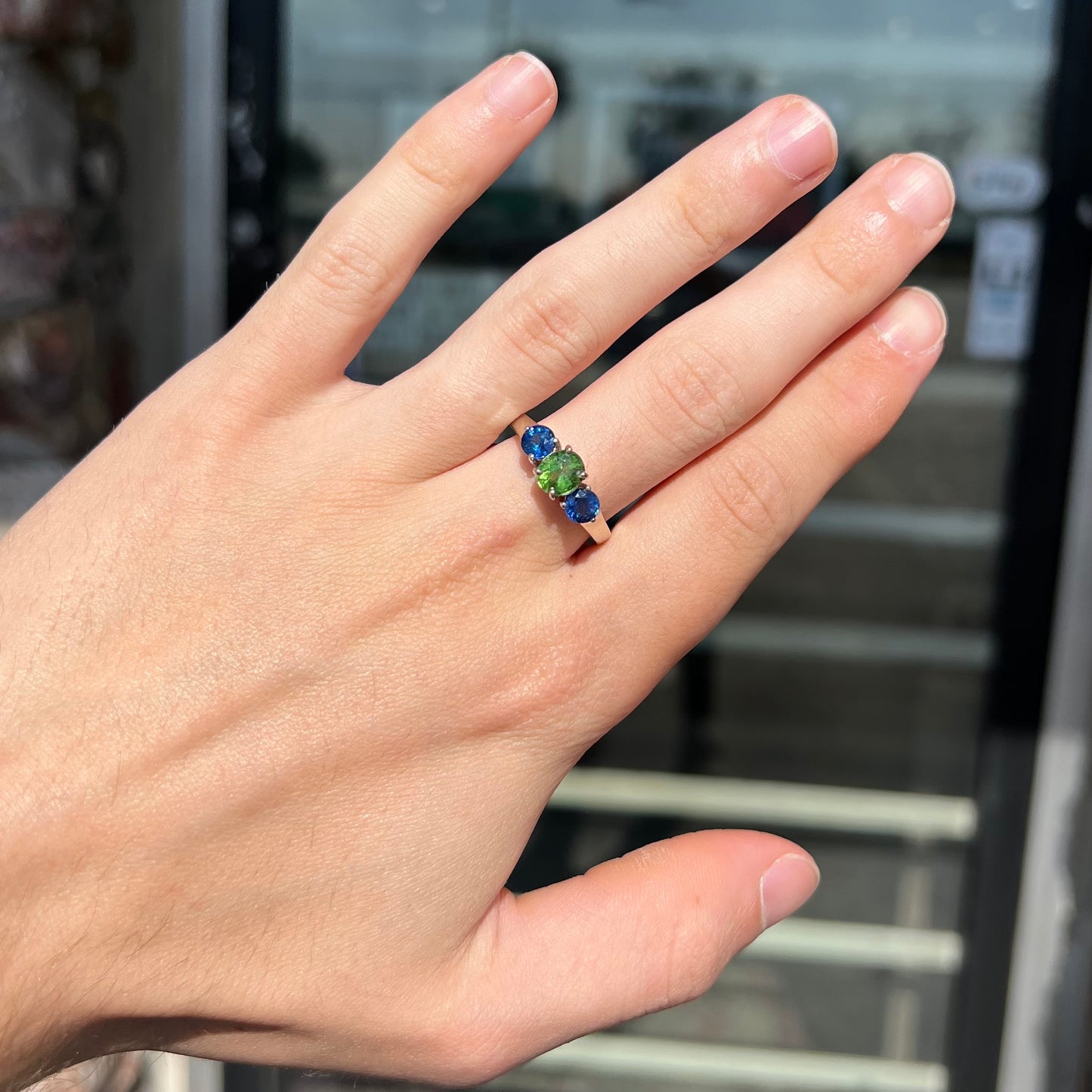 A ladies' white gold three stone ring set with two round blue sapphires and an oval cut green tsavorite garnet.