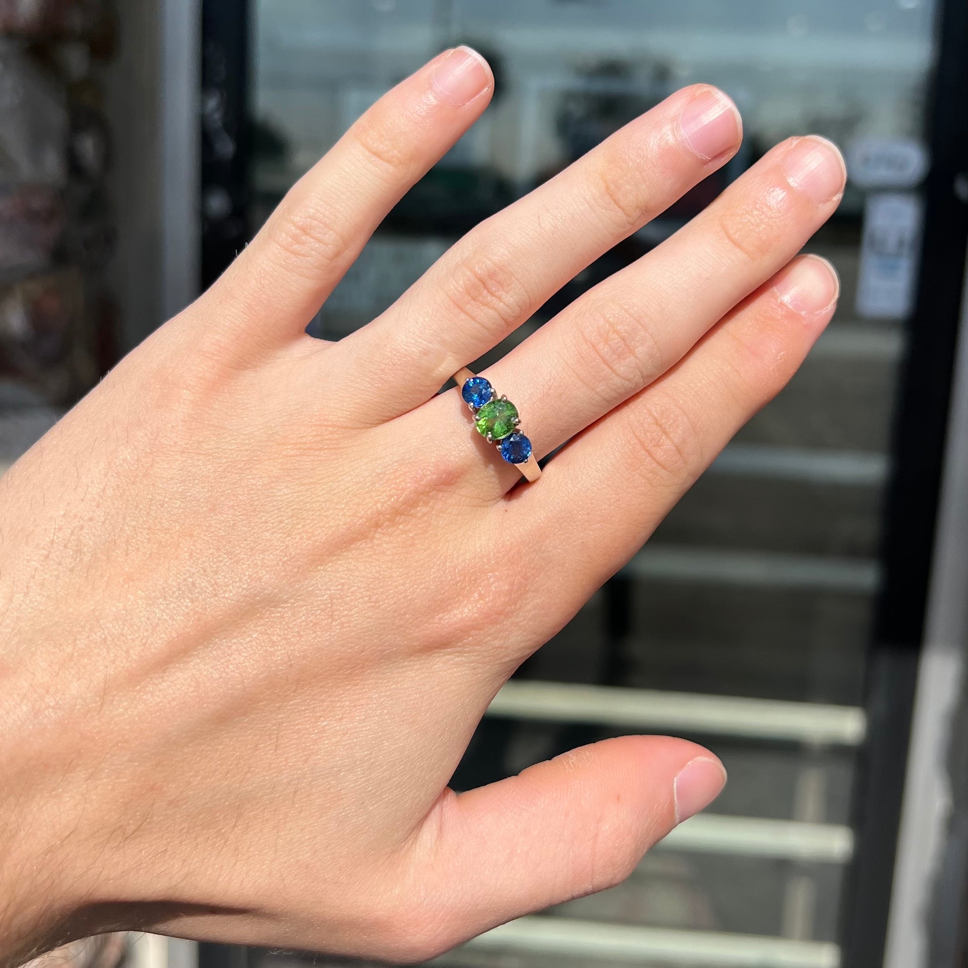 A ladies' white gold three stone ring set with two round blue sapphires and an oval cut green tsavorite garnet.