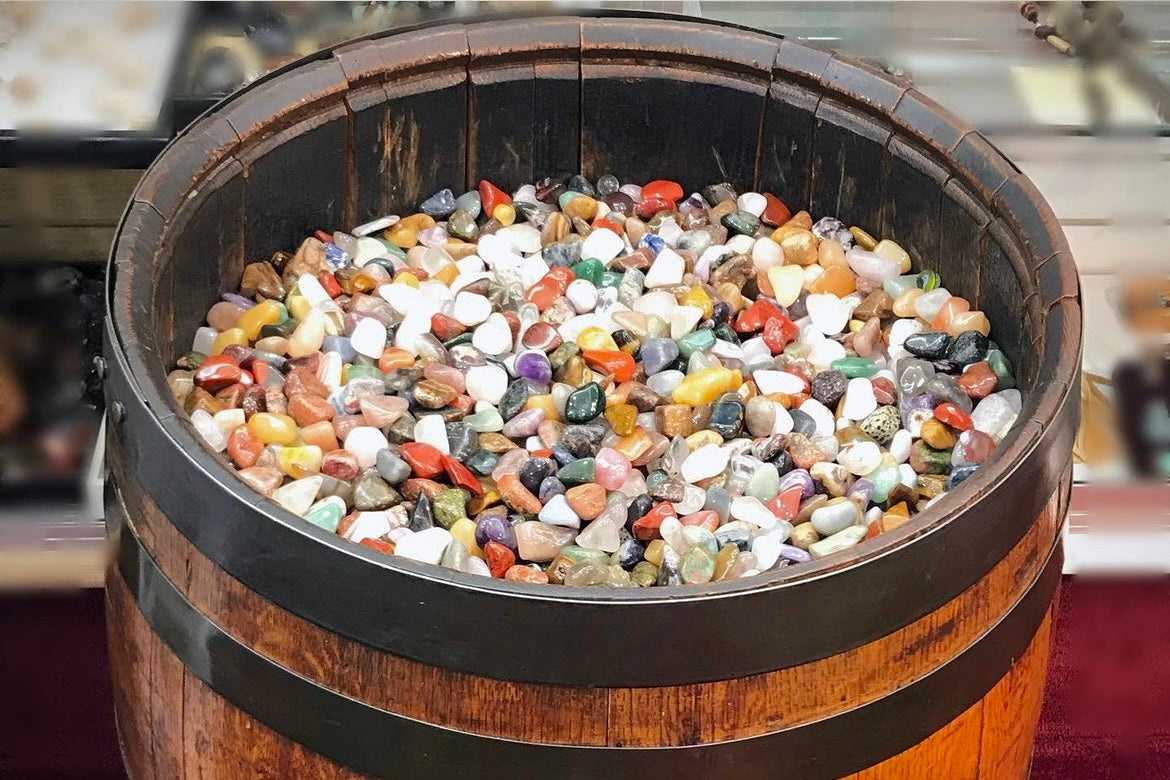 A rustic oak barrel filled with mixed varieties of natured tumbled stones.