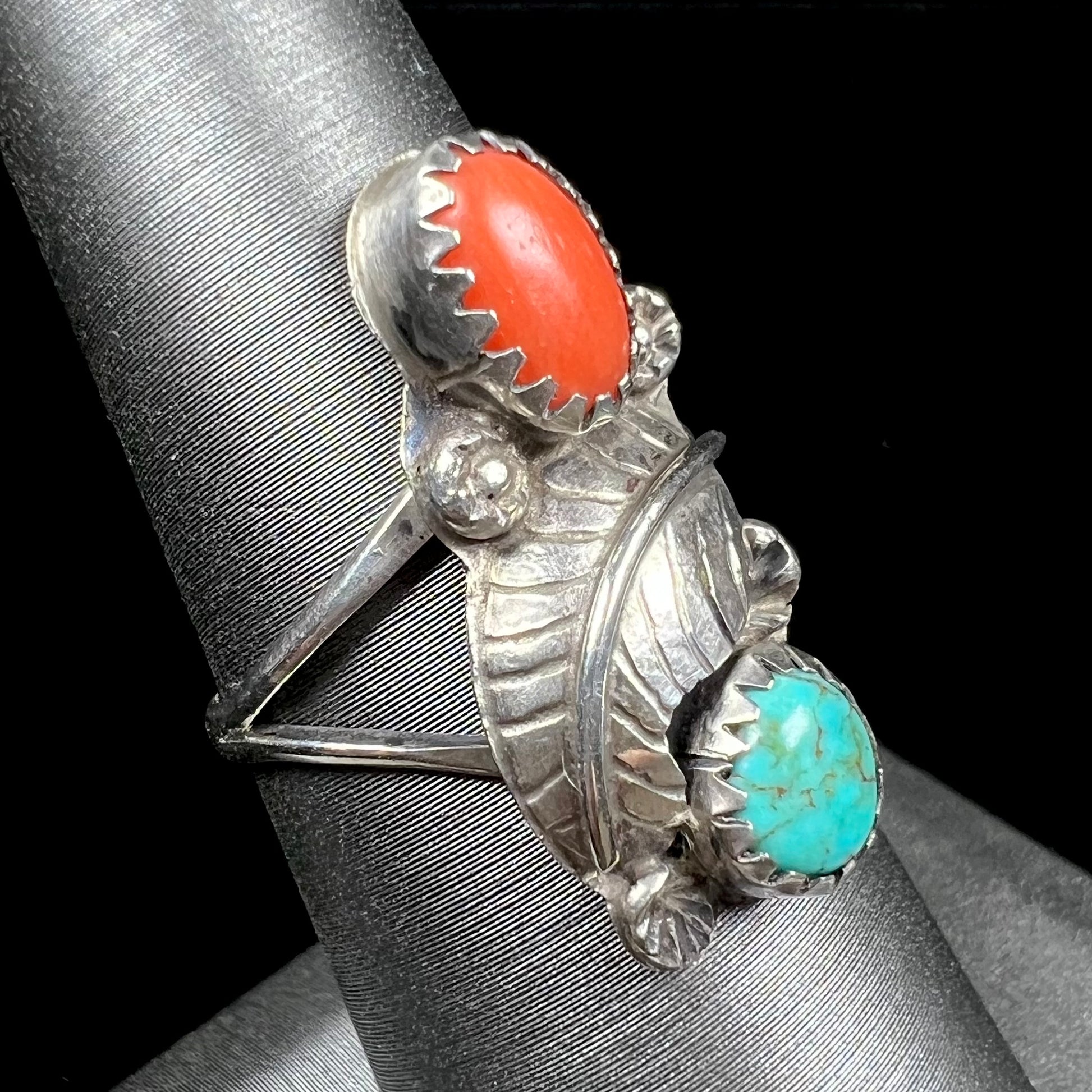 A vintage sterling silver Navajo style ring set with turquoise and coral stones and a feather design.