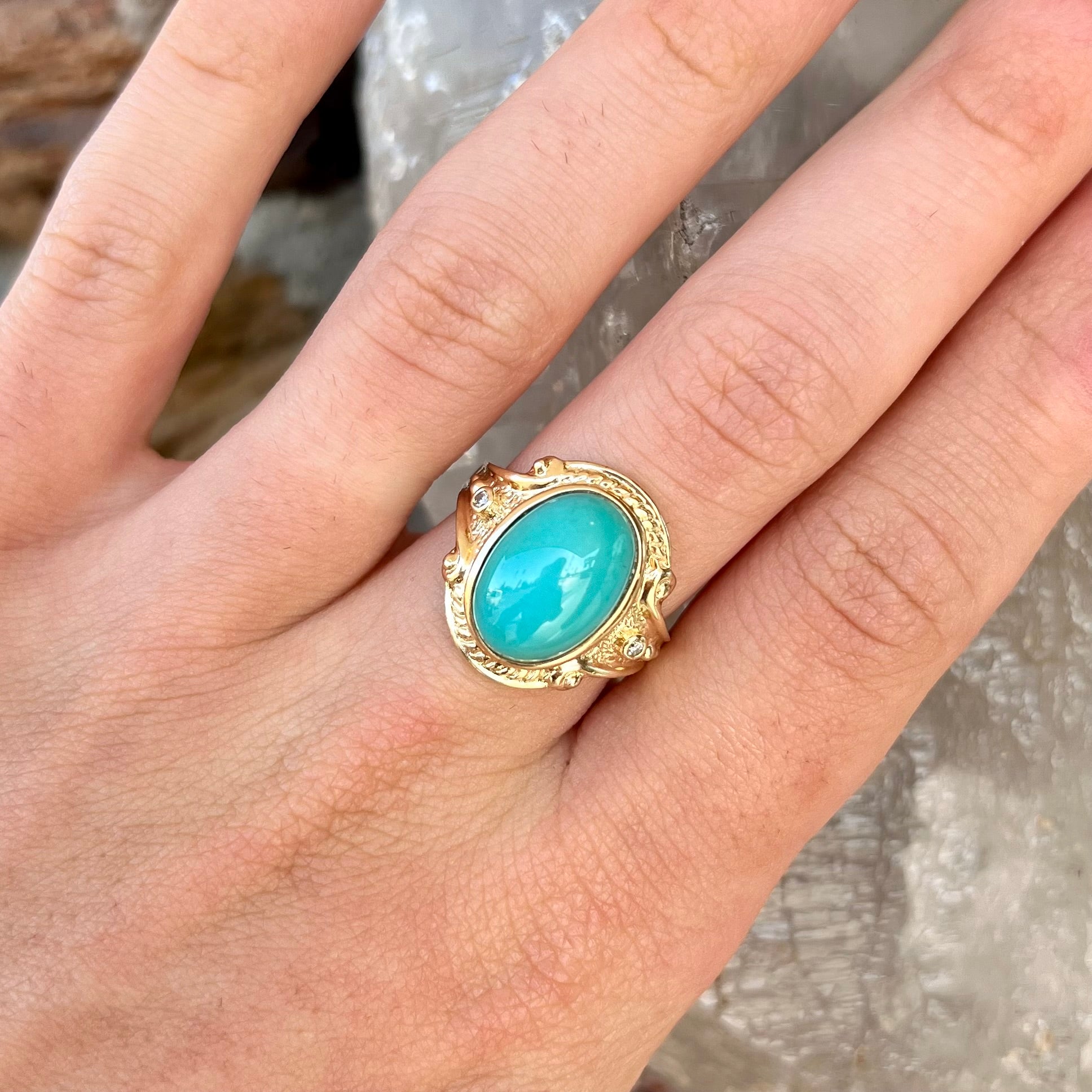 A yellow gold ring set with a greenish blue Sleeping Beauty turquoise cabochon with two diamond accents.