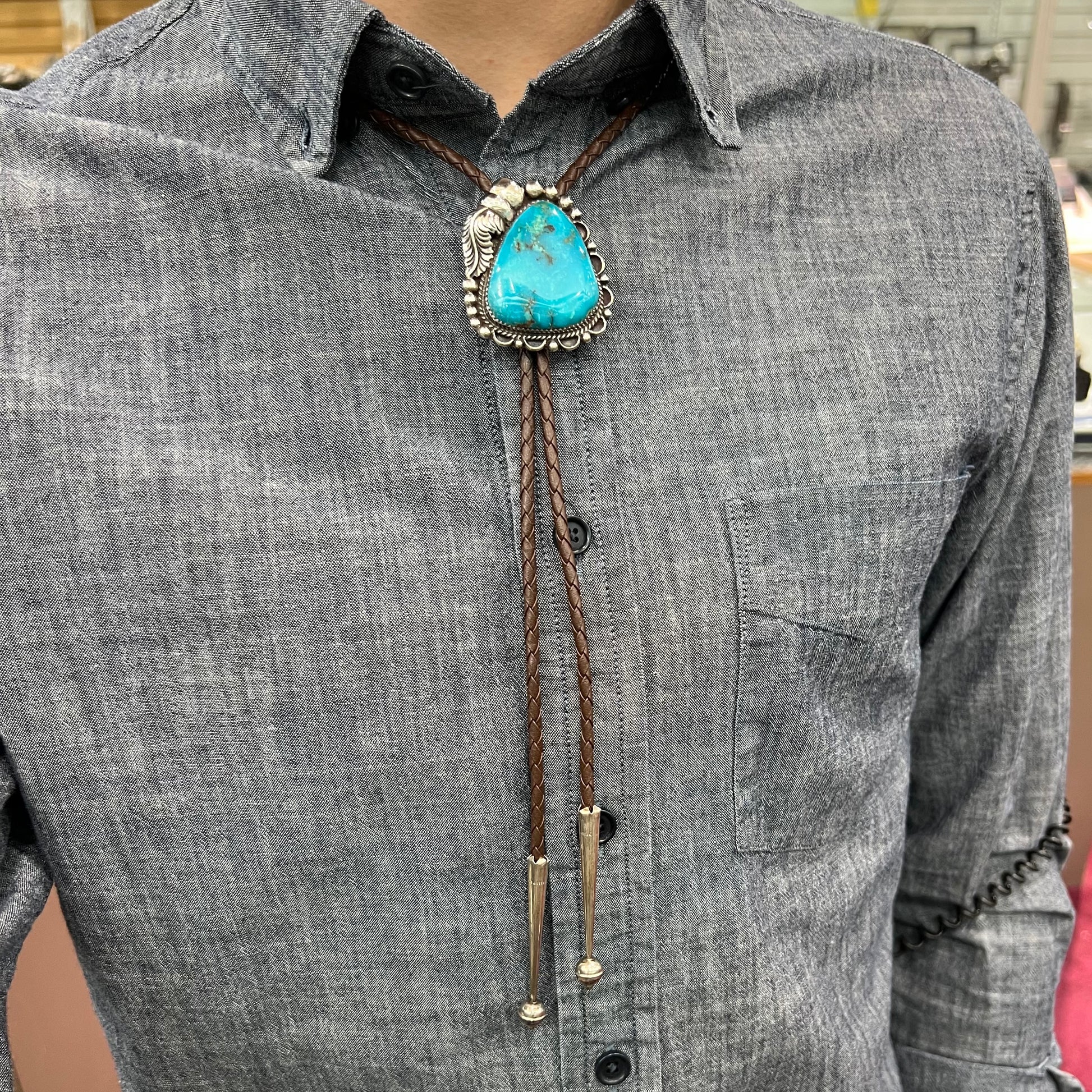 A men's sterling silver, Navajo style bolo tie set with a Pilot Mountain turquoise stone.  The rope is brown leather.