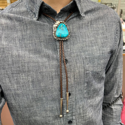 A men's sterling silver, Navajo style bolo tie set with a Pilot Mountain turquoise stone.  The rope is brown leather.