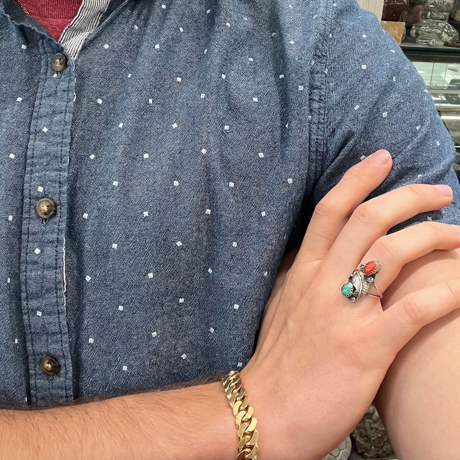 A vintage sterling silver Navajo style ring set with turquoise and coral stones and a feather design.