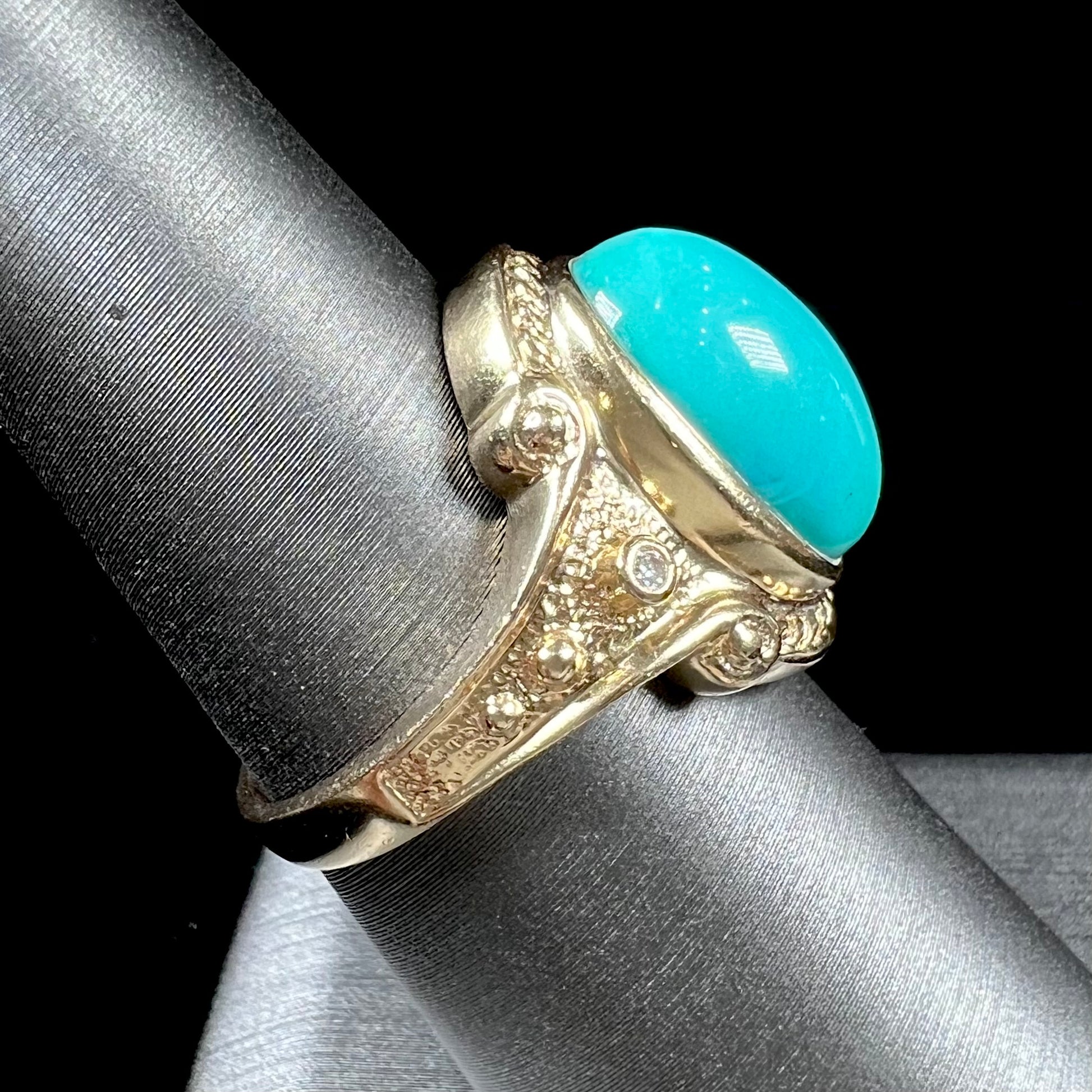 A yellow gold ring set with a greenish blue Sleeping Beauty turquoise cabochon with two diamond accents.