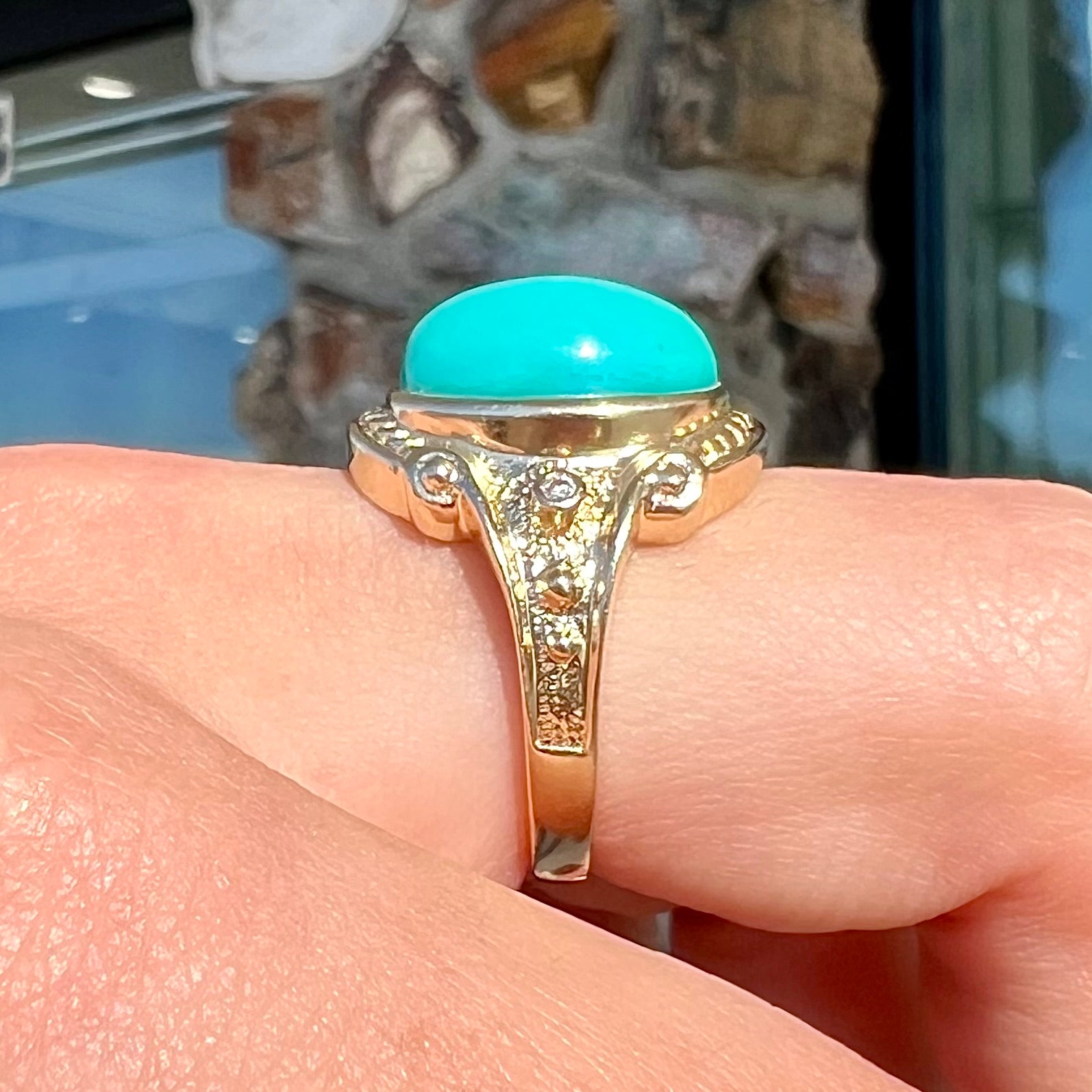 A yellow gold ring set with a greenish blue Sleeping Beauty turquoise cabochon with two diamond accents.