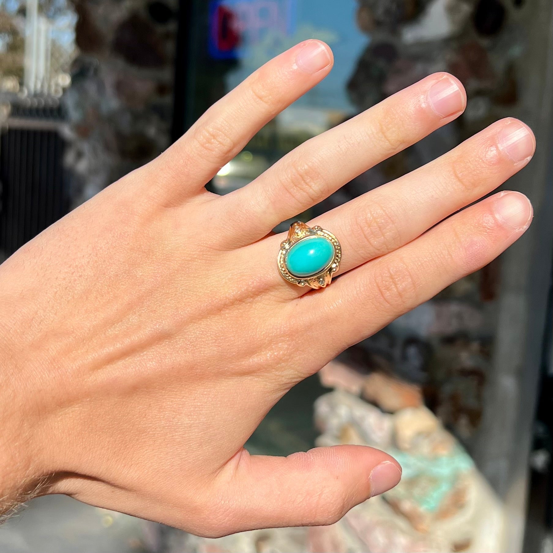 A yellow gold ring set with a greenish blue Sleeping Beauty turquoise cabochon with two diamond accents.