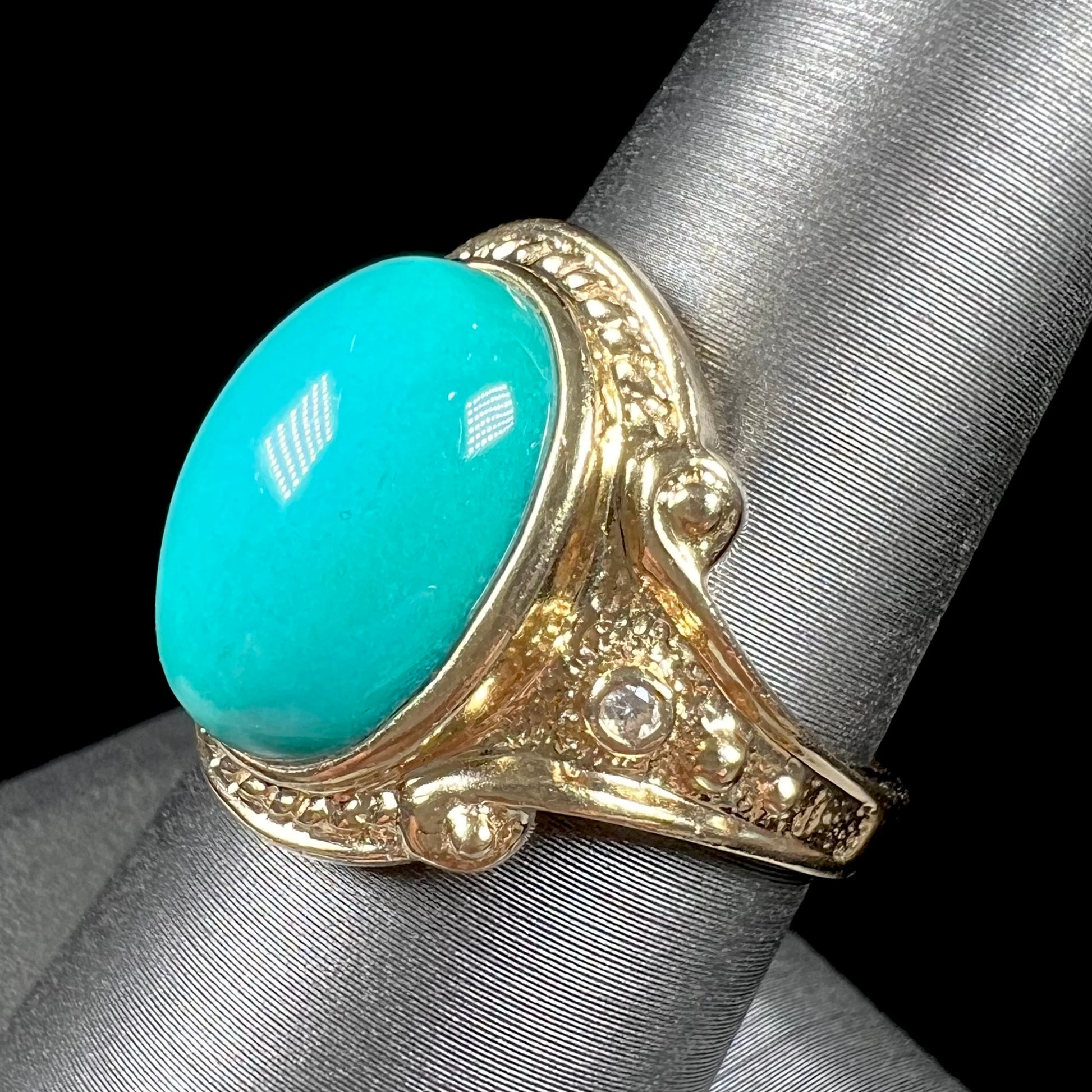 A yellow gold ring set with a greenish blue Sleeping Beauty turquoise cabochon with two diamond accents.