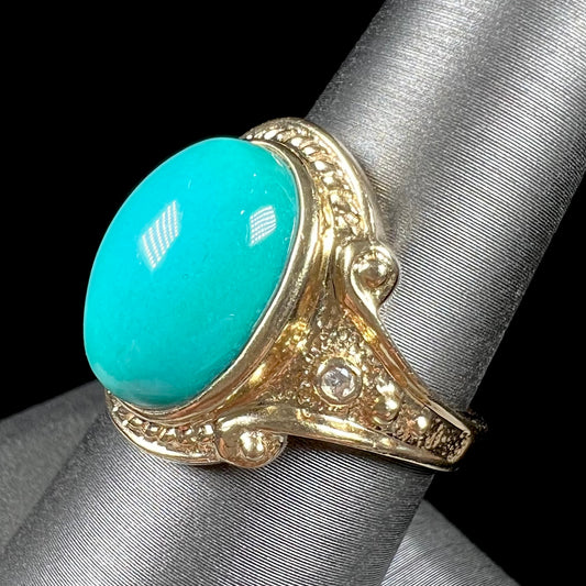 A yellow gold ring set with a greenish blue Sleeping Beauty turquoise cabochon with two diamond accents.