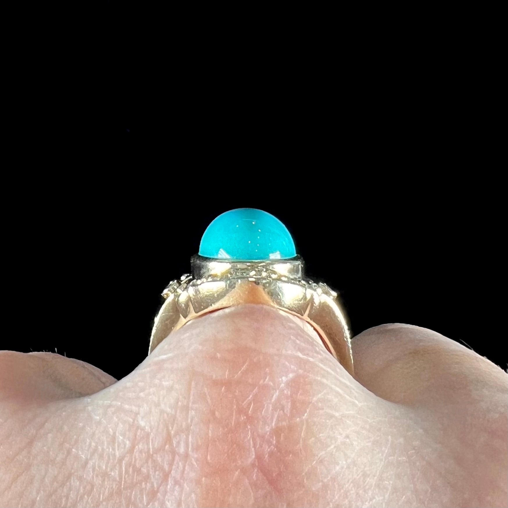 A yellow gold ring set with a greenish blue Sleeping Beauty turquoise cabochon with two diamond accents.